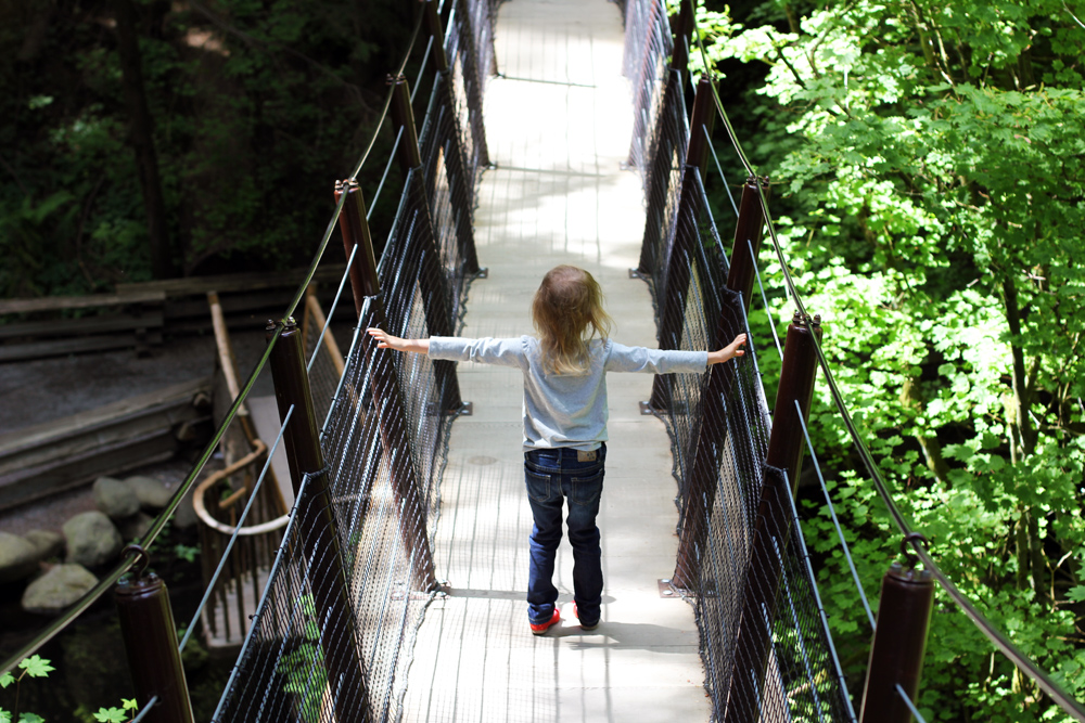 girl keeping balance on suspension bridge between trees